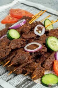 Nigerian street food, Suya, featuring spicy grilled beef skewers served with fresh onions and tomatoes